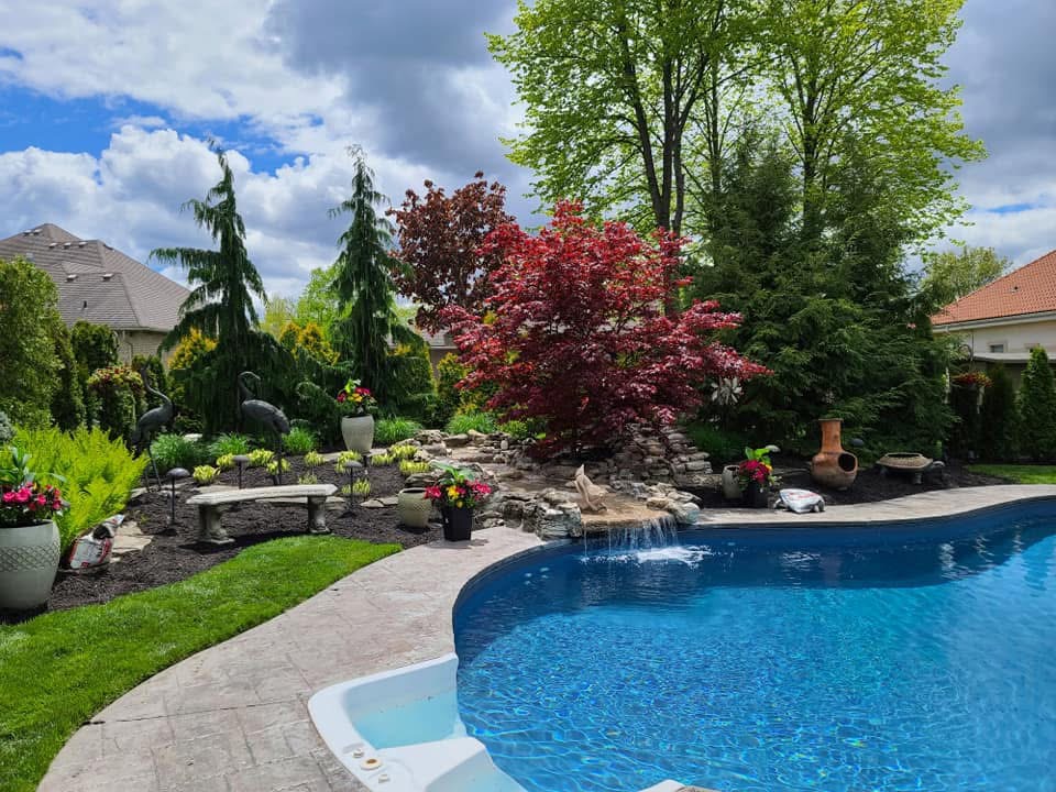 Landscaped backyard pool with waterfall, trees, and garden beds