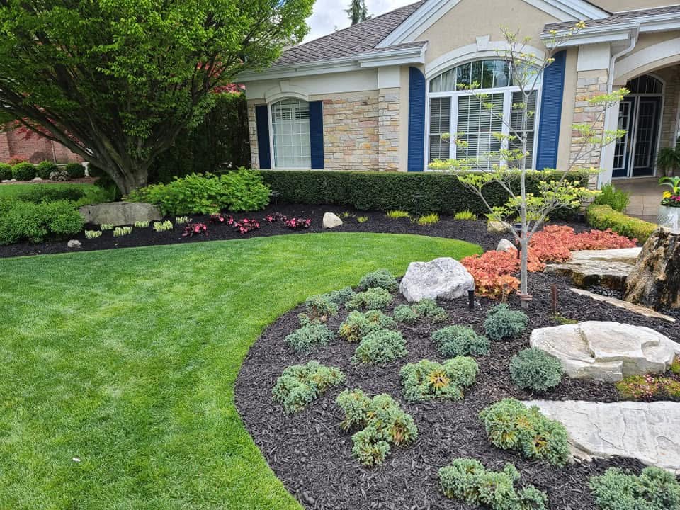 Manicured front lawn with sculpted beds, shrubs, and natural stone
